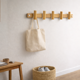 Tote bag hanging on a wooden hook against a white wall with a room in the background.