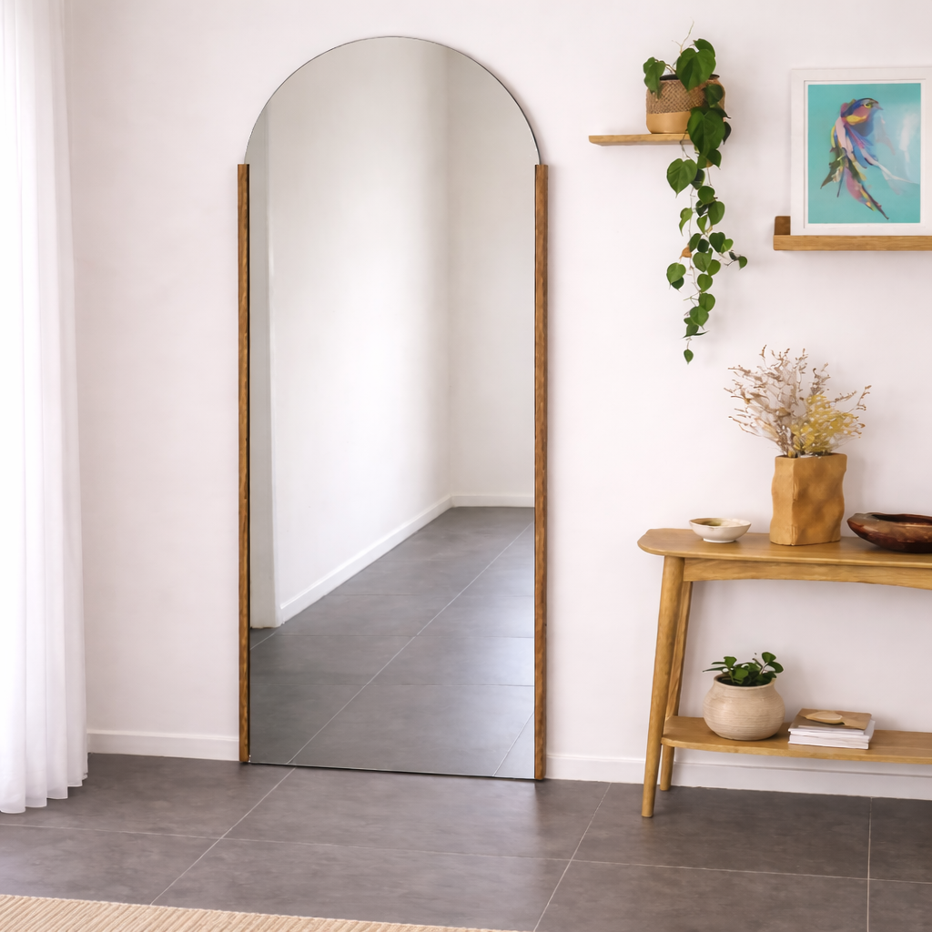 Arched floor mirror with wooden frame in a room with a small table and decorative items.
