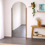 Arched floor mirror with wooden frame in a room with a small table and decorative items.