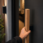 Hand opening a modern door with a wooden handle in a well-lit interior setting.