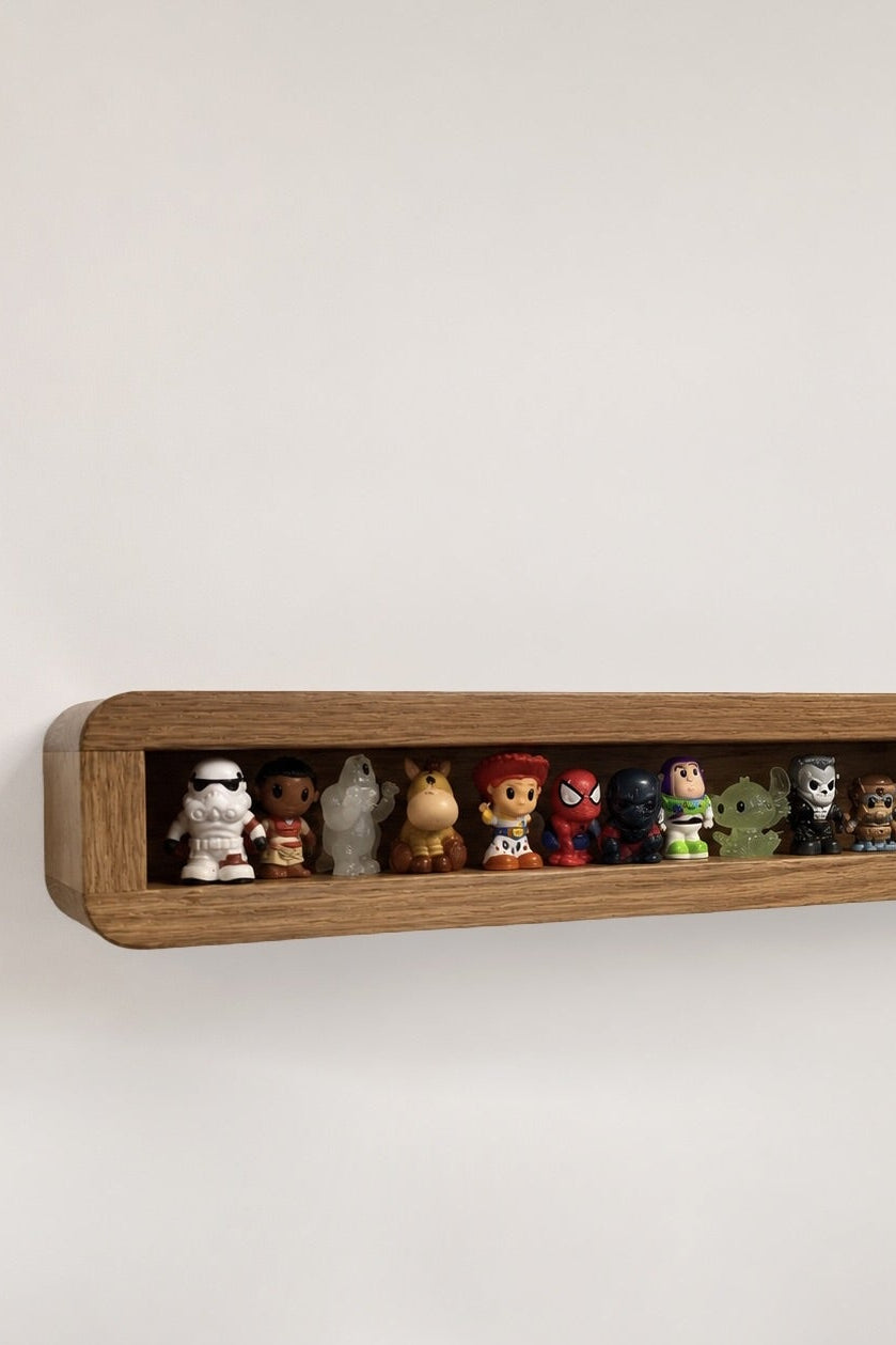 A long, narrow wooden wall shelf mounted on a plain light wall, holding a row of small collectible figurines and toys.