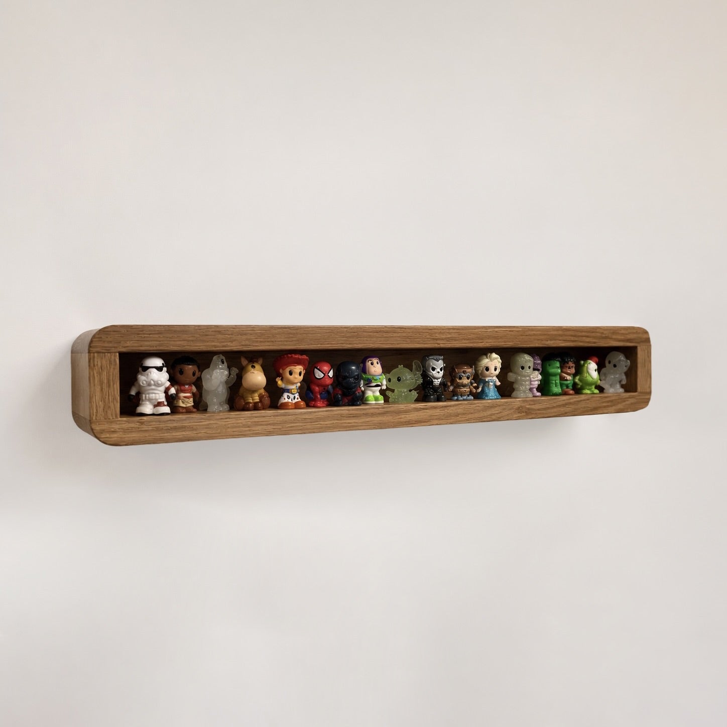 A long, narrow wooden wall shelf mounted on a plain light wall, holding a row of small collectible figurines and toys.