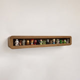 A long, narrow wooden wall shelf mounted on a plain light wall, holding a row of small collectible figurines and toys.